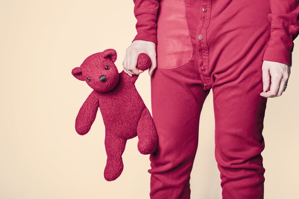Photograph of a child in red pajamas holding a red teddy bear