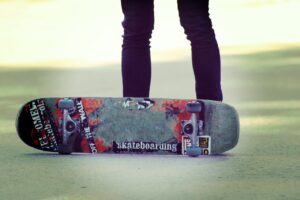 Photograph of a skateboard on its side with the legs of a person standing behind it