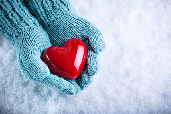 Hand with mitten holding a red heart over snow.